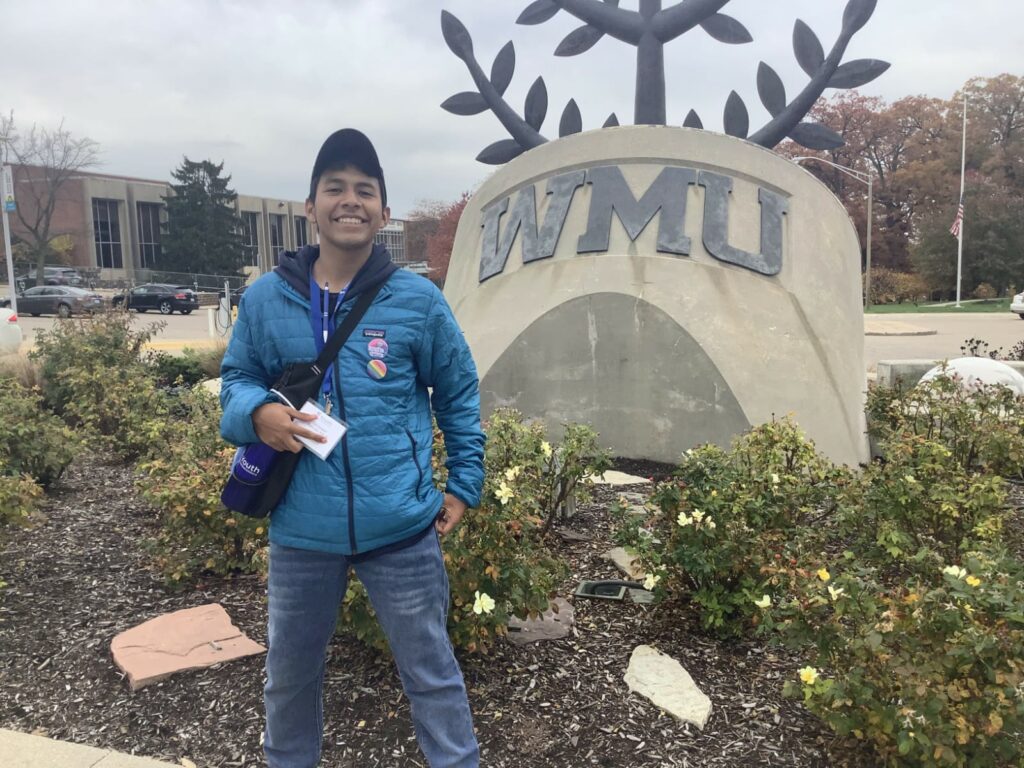 A young adult stands in front of a statue with the letters "WMU" on it.