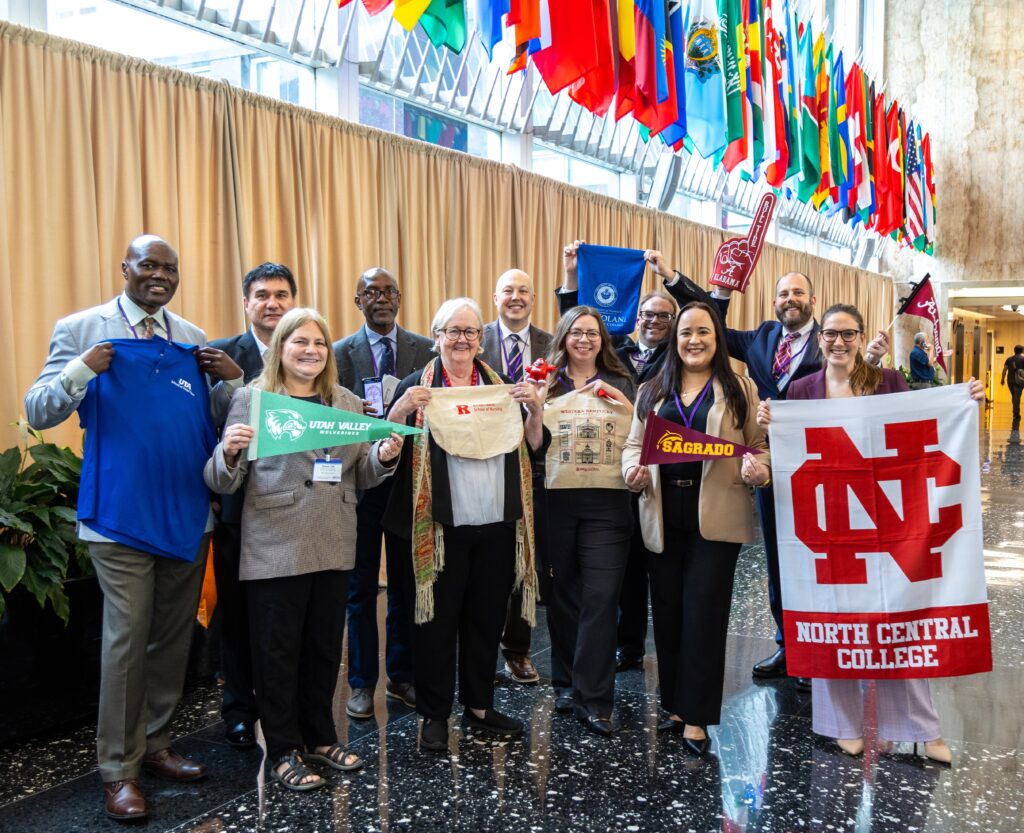 Eleven adults pose as a group while holding merchandise from the different universities they represented at the symposium.